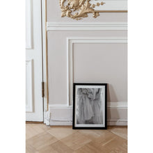 Load image into Gallery viewer, black and white fine art print, close up of hands holding tulle skirt, softness, fine art print in black frame on floor leaning against ornamental wall with gold, French interior