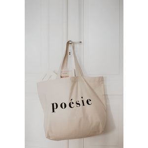 natural organic bag with the word poésie printed in large letters in middle, hanging from a door handle against white door, tow French books inside, Gallimard and Astier de Villatte