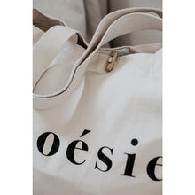Load image into Gallery viewer, close up of natural organic tote bag partially showing poésie text printed in black on the side, sturdy handles and wooden toggle closure

