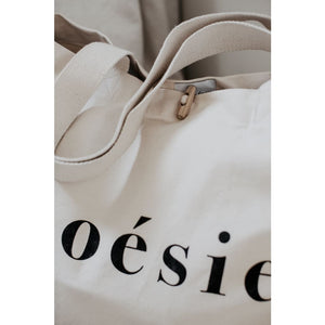close up of natural organic tote bag partially showing poésie text printed in black on the side, sturdy handles and wooden toggle closure